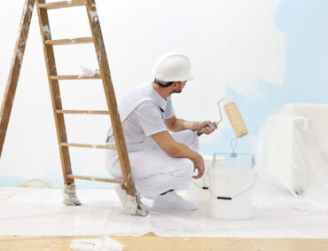 painter man at work takes the color with paint roller from the bucket
